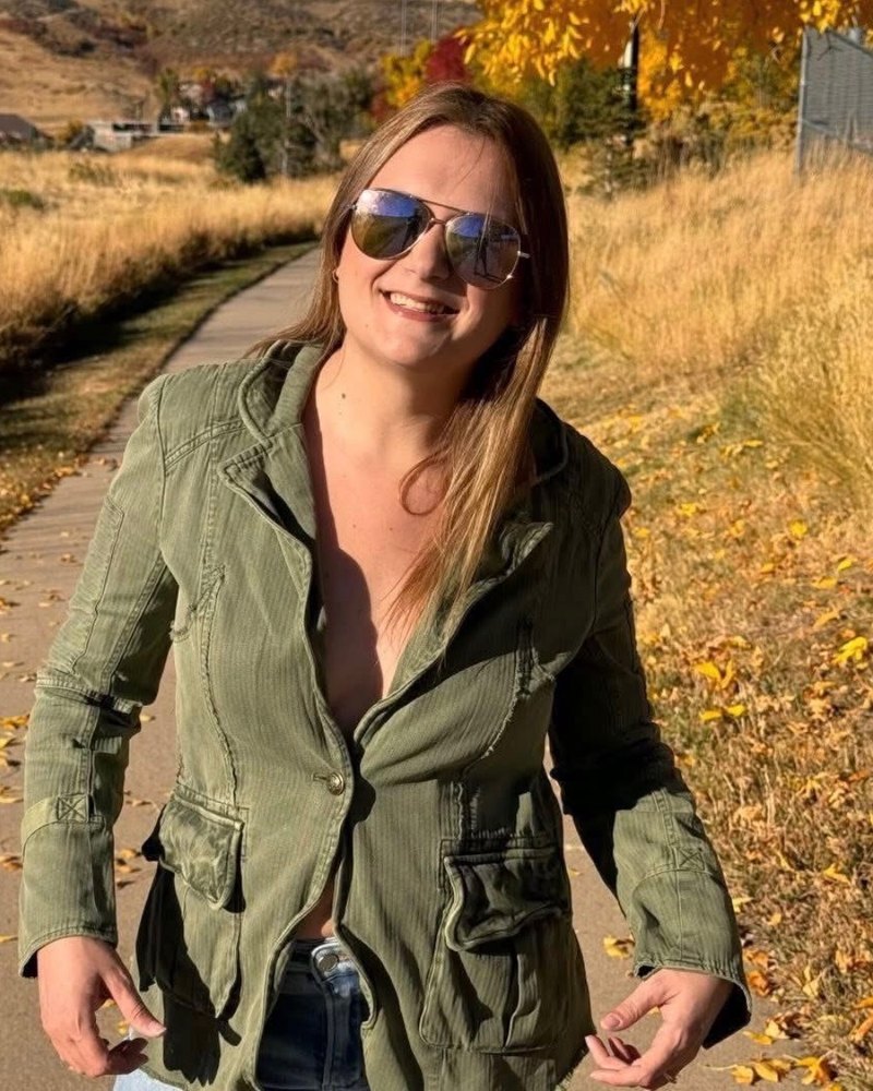 Crystal Rose Reynolds smiling in sunglasses and a green jacket on a fall path lined with golden grass
